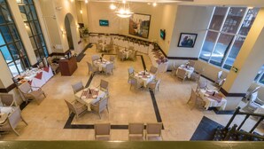 Un amplio vestíbulo de hotel con varias zonas de restauración, una escalera central y grandes ventanales que ofrecen luz natural.
