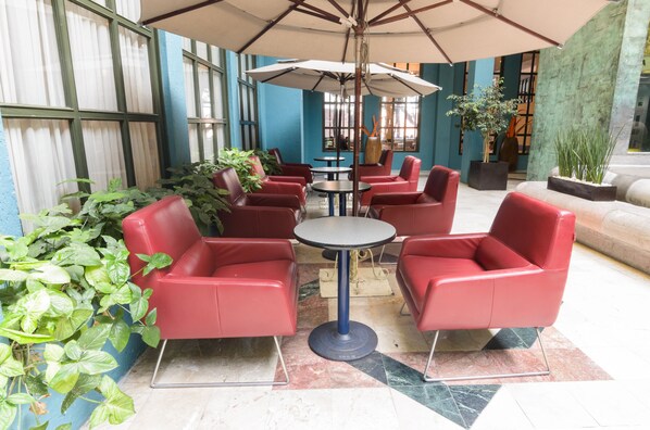 A seating area with red chairs and tables, surrounded by potted plants and large umbrellas. - Hotel San Francisco Leon (León)