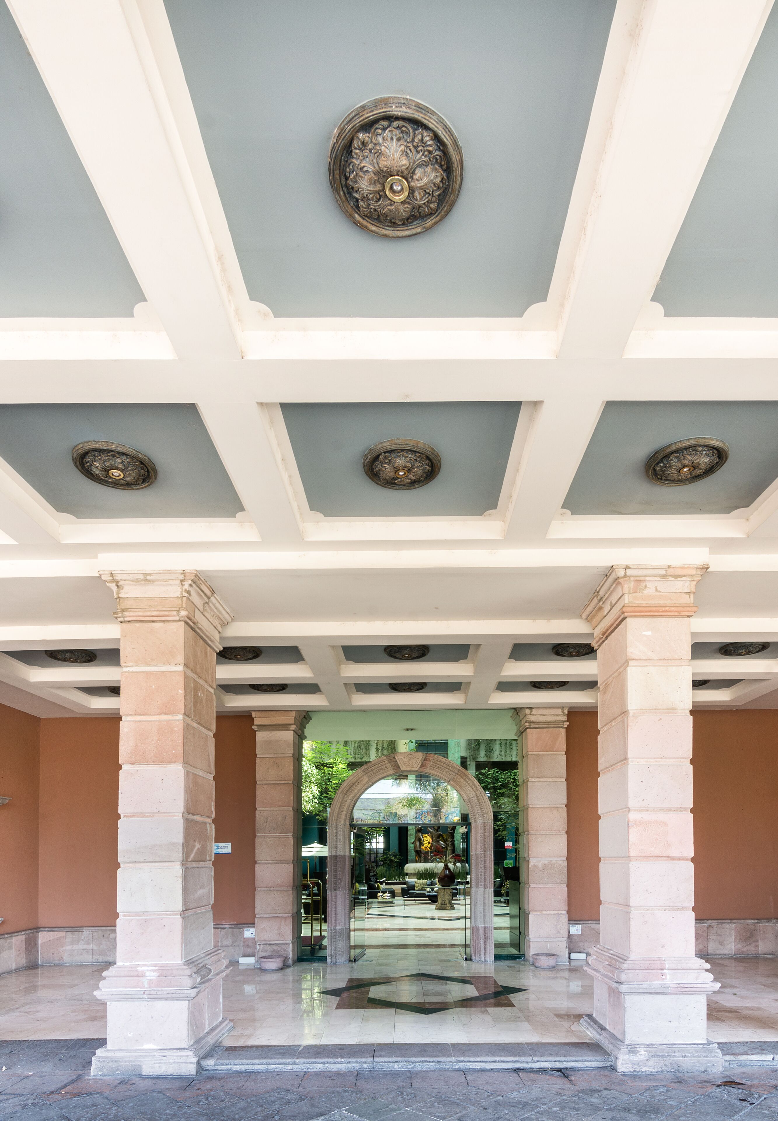 A covered entrance with a central archway, columns, and decorative ceiling medallions.