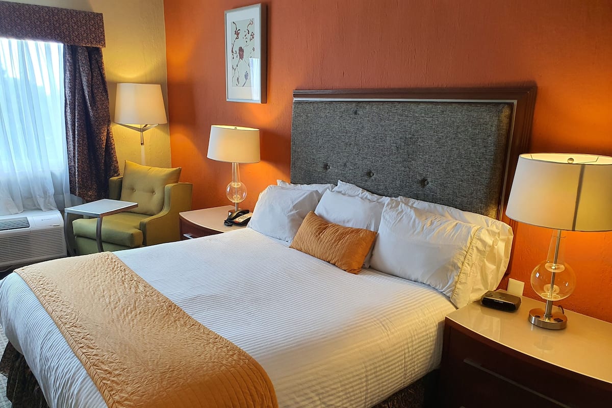 Ein Hotelzimmer mit einem großen Bett, Nachttischen, einem Sessel, einem Schreibtisch und einem Wandbild.