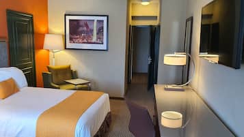 A hotel room with a large bed, a desk, a chair, a TV, and a framed picture on the wall.