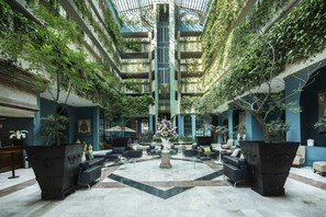 A spacious atrium with a central staircase, surrounded by seating areas and potted plants. - Hotel San Francisco Leon (León)
