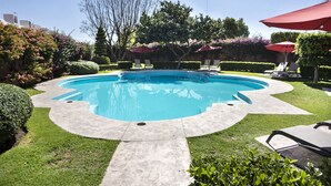 Una piscina rodeada de céspedes cuidados, sombrillas rojas y setos perfectamente recortados.
