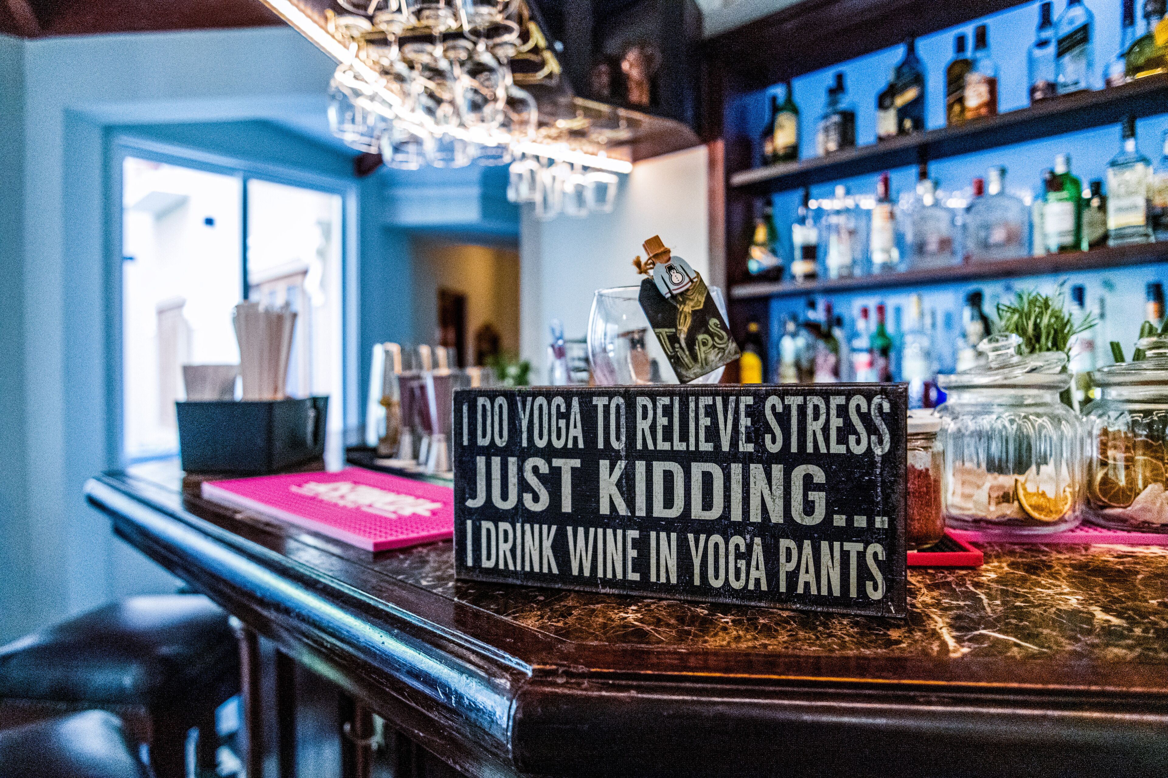 Una barra con un letrero que dice: "Hago yoga para aliviar el estrés, ¡es broma!... Tomo vino con ropa de yoga.