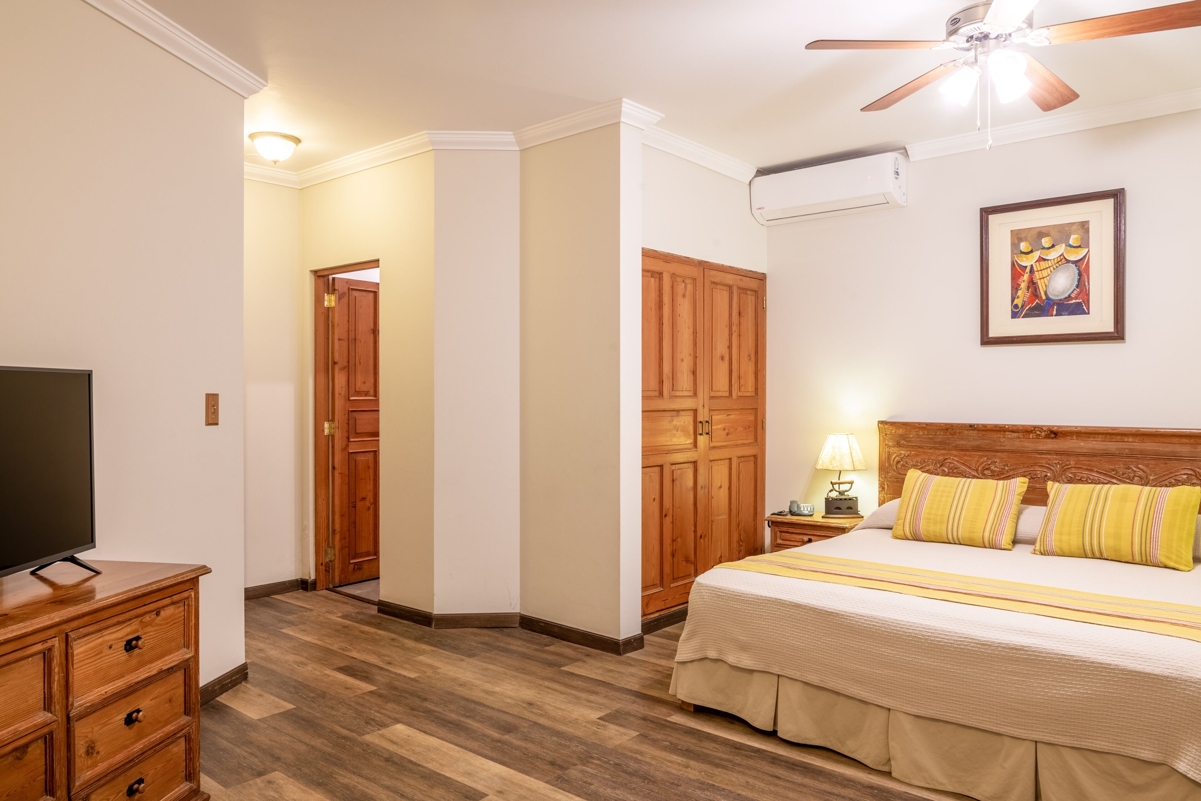 A hotel room with a bed, wooden wardrobe, a television, and a ceiling fan.