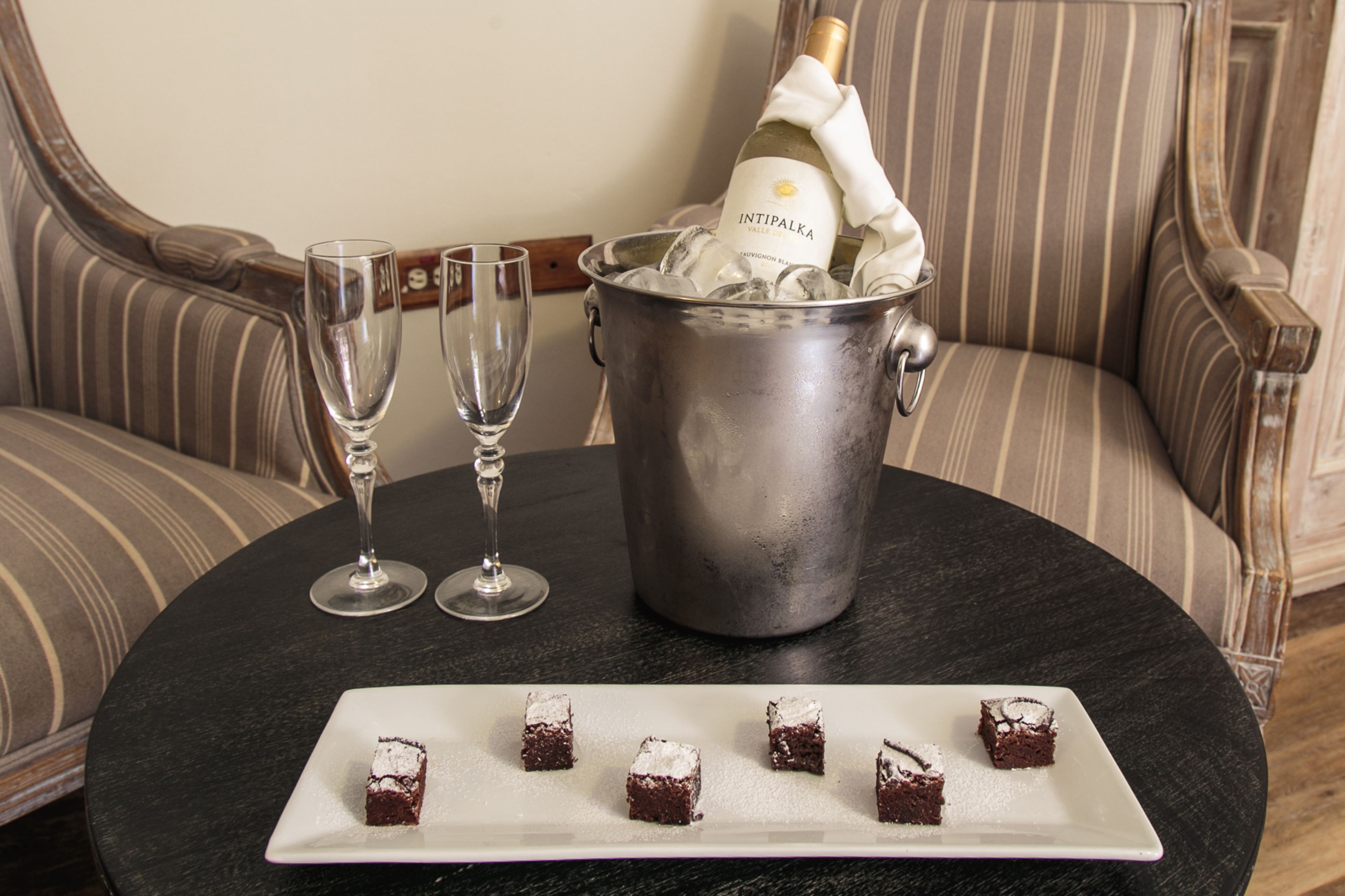 A table with a bottle of champagne, ice, and glasses, and a plate with dessert cubes.
