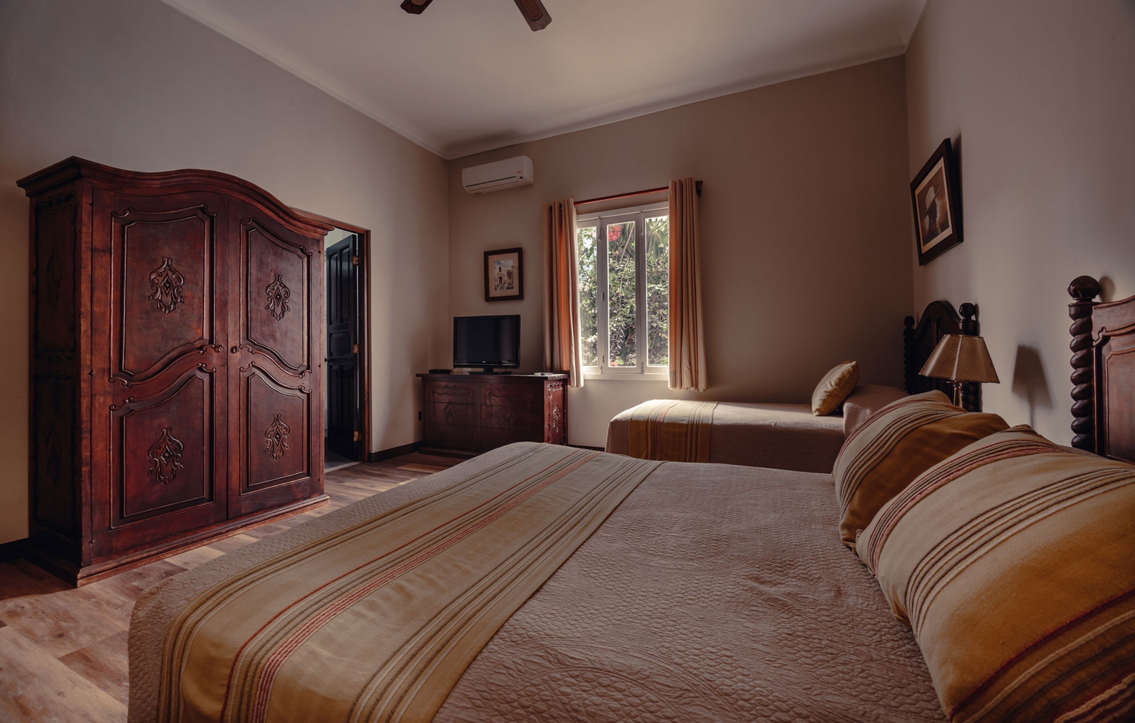 Een slaapkamer met een groot bed, een kledingkast, een televisie en een raam met gordijnen.