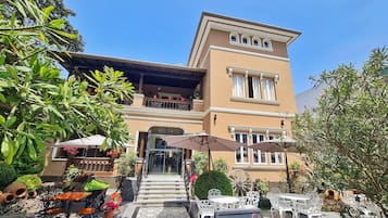 Two-story building with a flat roof and balcony, featuring a beige facade and outdoor seating area.
