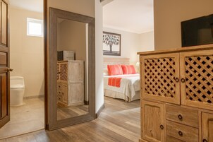 Un dormitorio con un armario de madera, una cama con ropa de cama naranja, una mesita de noche y un televisor instalado en la pared.