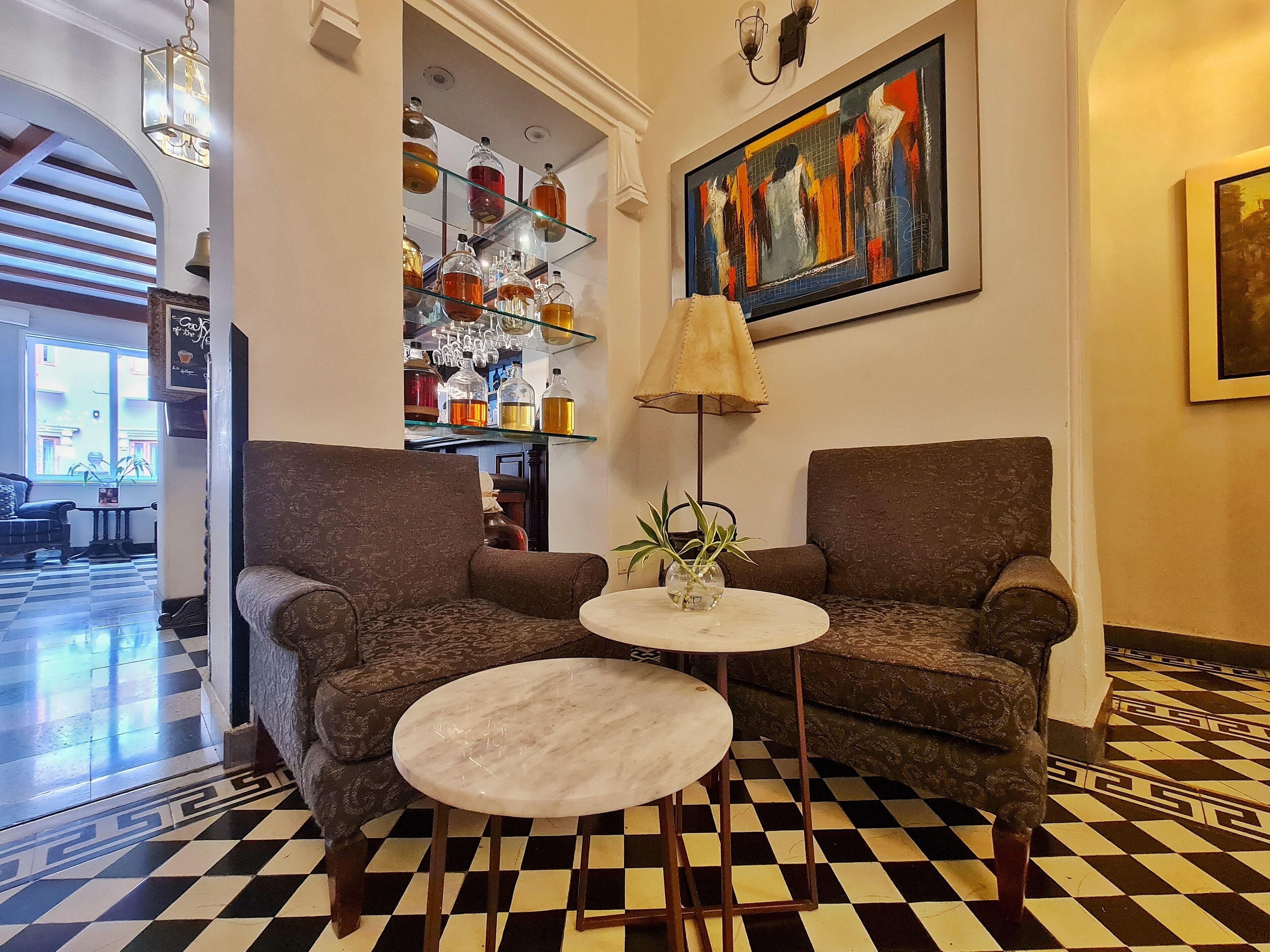 A lobby with two armchairs, a small round table, a floor lamp, and a painting on the wall.