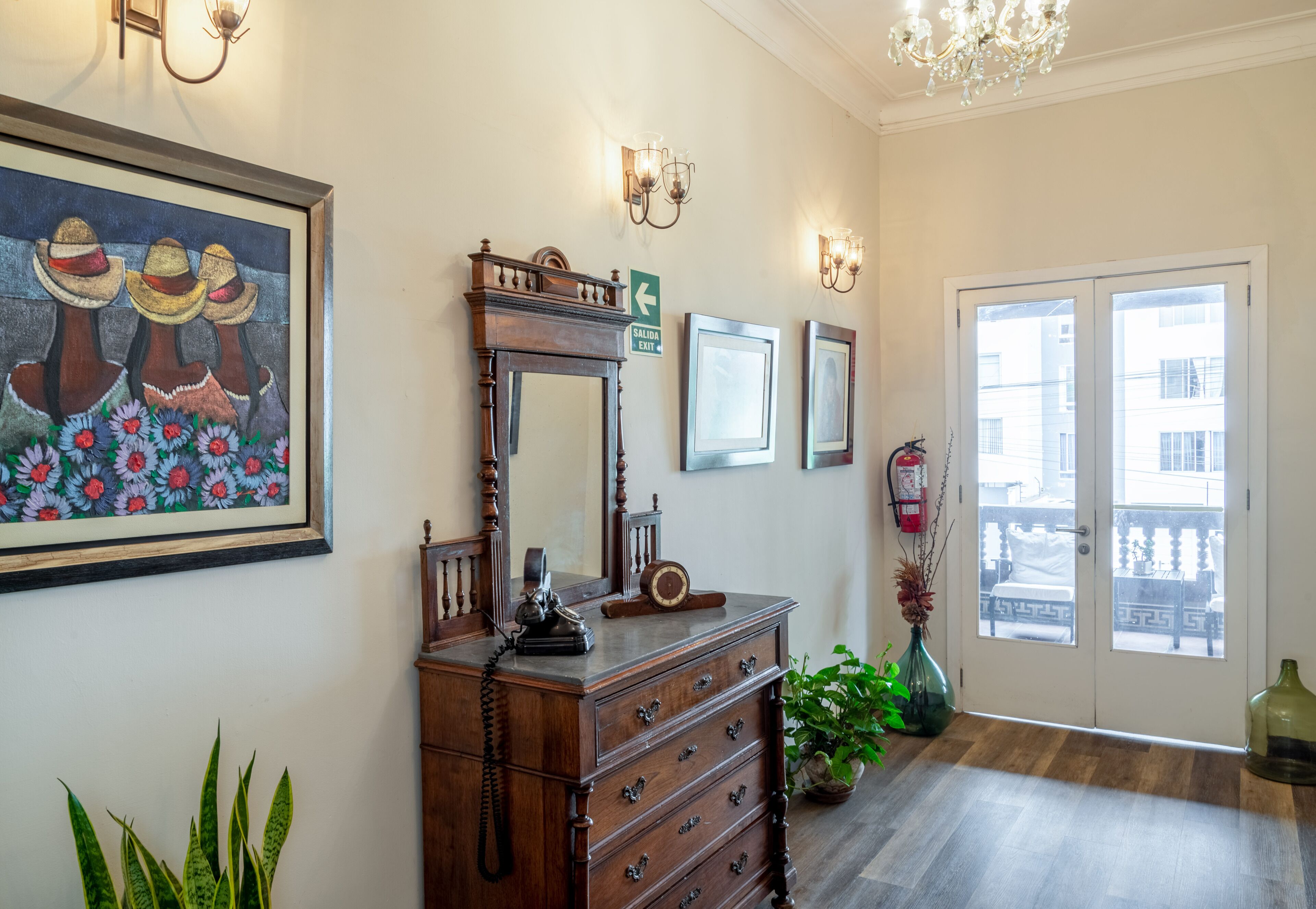 A hallway with a wooden dresser, framed artwork, wall sconces, and a door leading to a balcony.