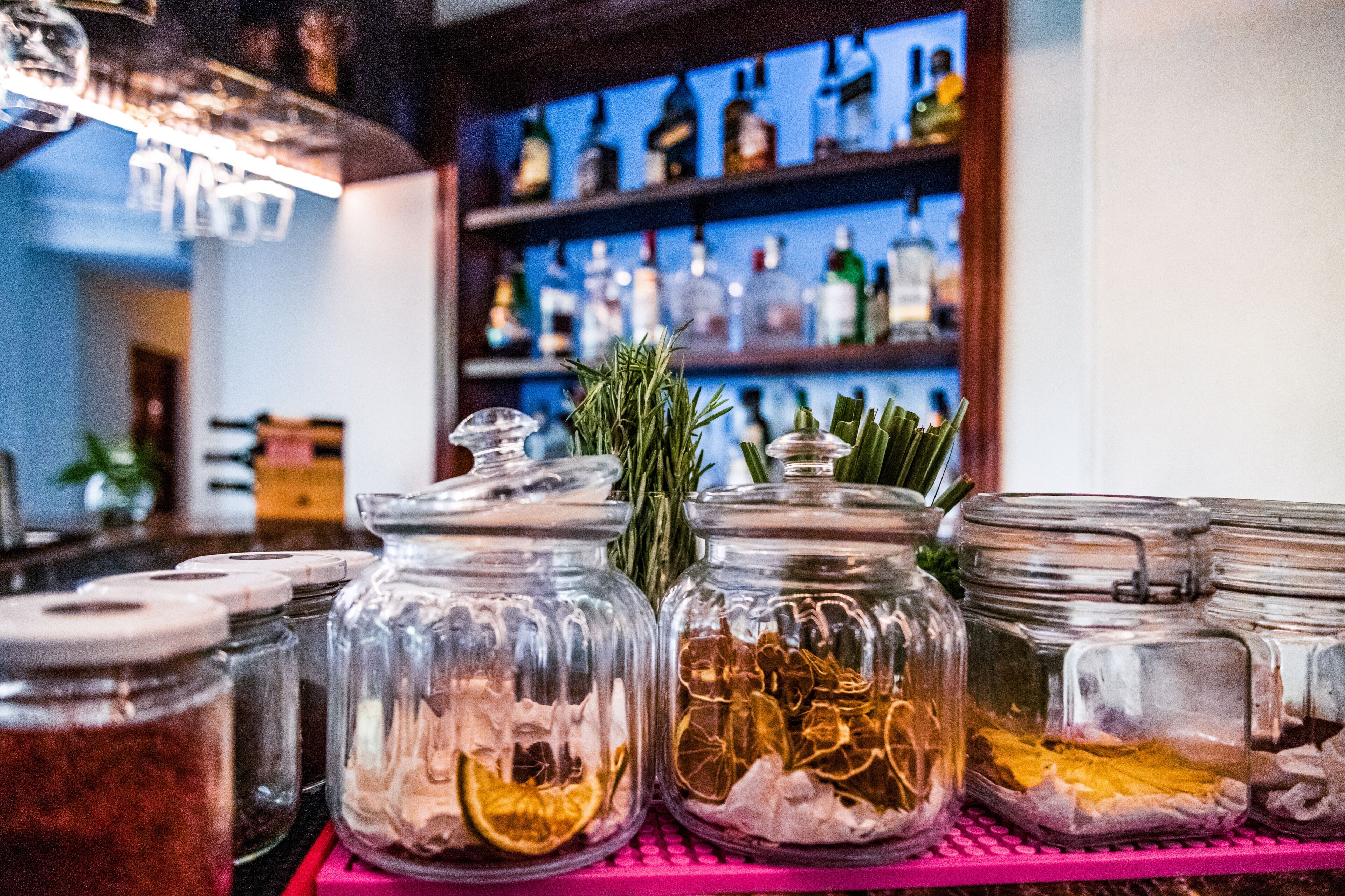 A bar area with glass jars containing various ingredients on a pink shelf.