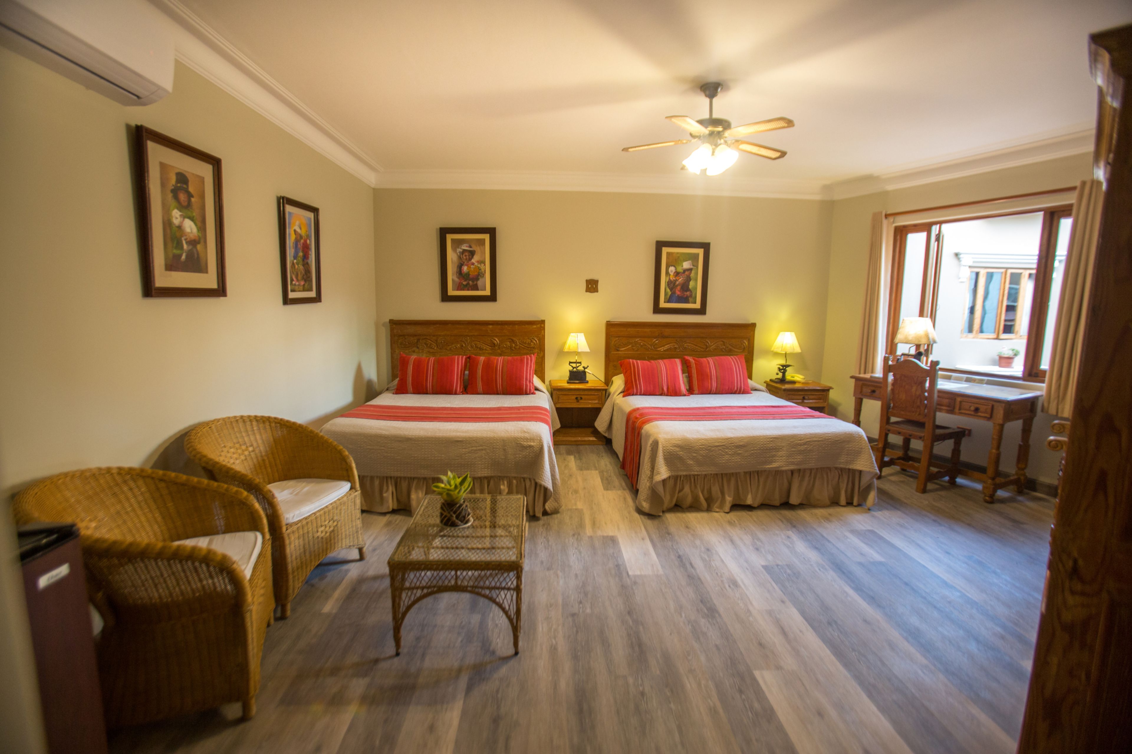 Een hotelkamer met twee bedden, een bureau, een stoel, rieten meubels en ingelijste foto's aan de muur.