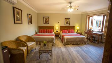 A hotel room with two beds, a desk, a chair, wicker furniture, and framed pictures on the walls.