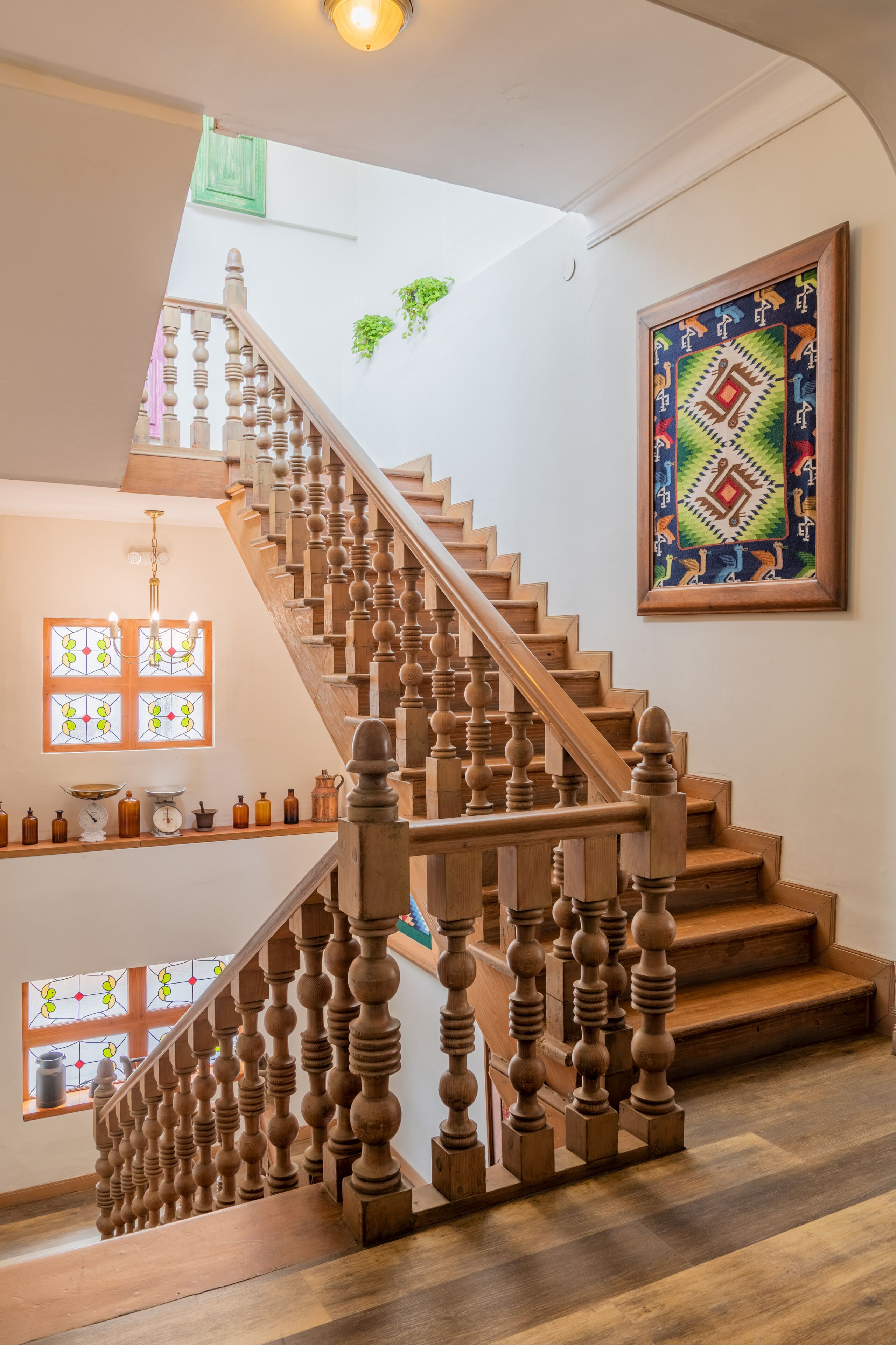 A wooden staircase with a balustrade, a chandelier, and a wall-mounted artwork.
