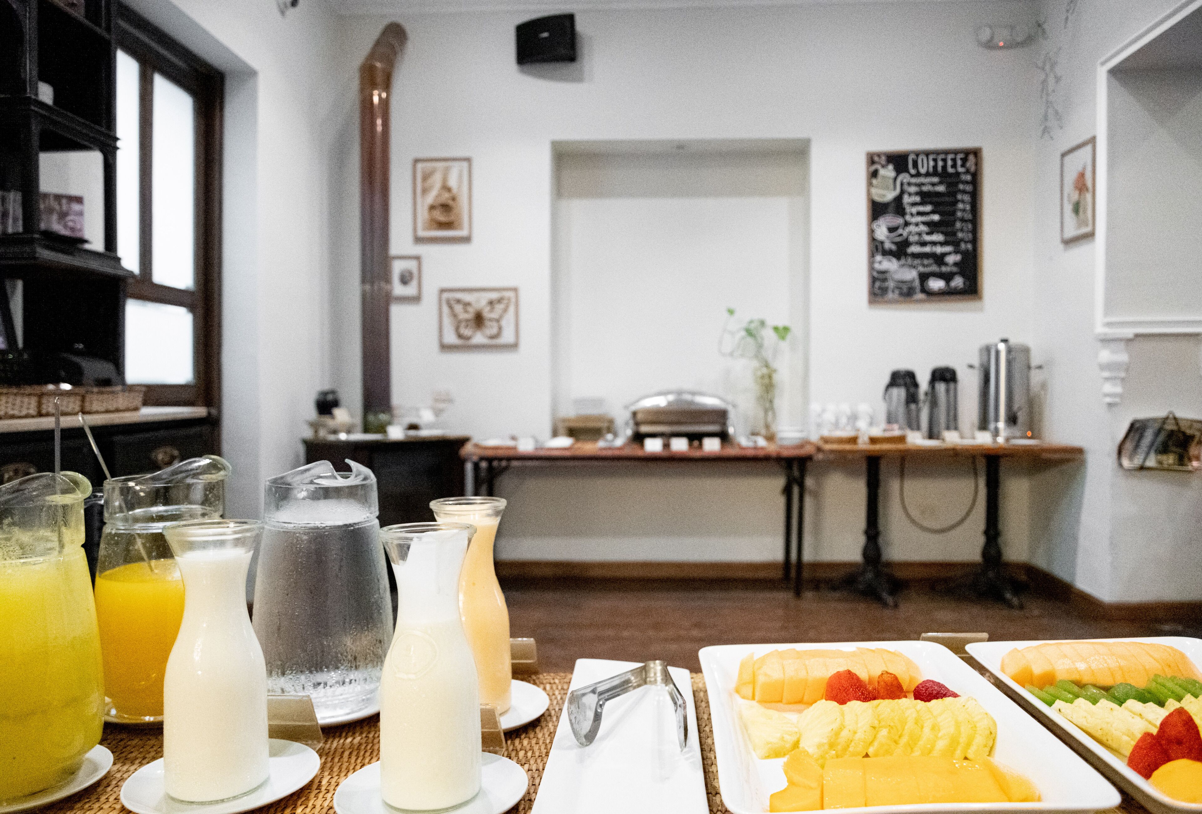 A breakfast setting with various beverages and fruit on plates, a coffee menu on the wall, and a counter with coffee machines.