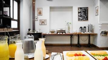 A breakfast setting with various beverages and fruit on plates, a coffee menu on the wall, and a counter with coffee machines.
