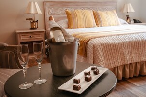 A hotel room with a bed, bedside tables, a nightstand, a lamp, a bucket with a bottle, and a plate with food.