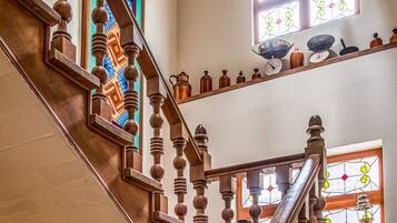 Una escalera de madera con un candelabro, vidrieras y estantes con adornos.