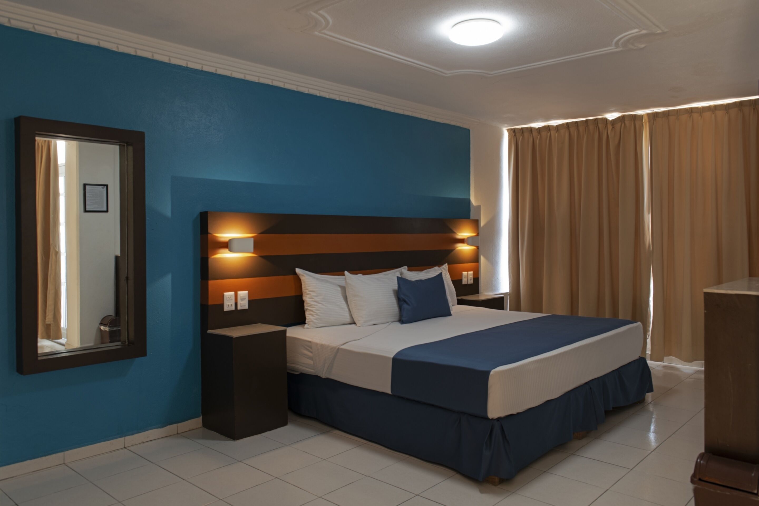 A hotel room with a large bed, a nightstand, a mirror, and a window with curtains.