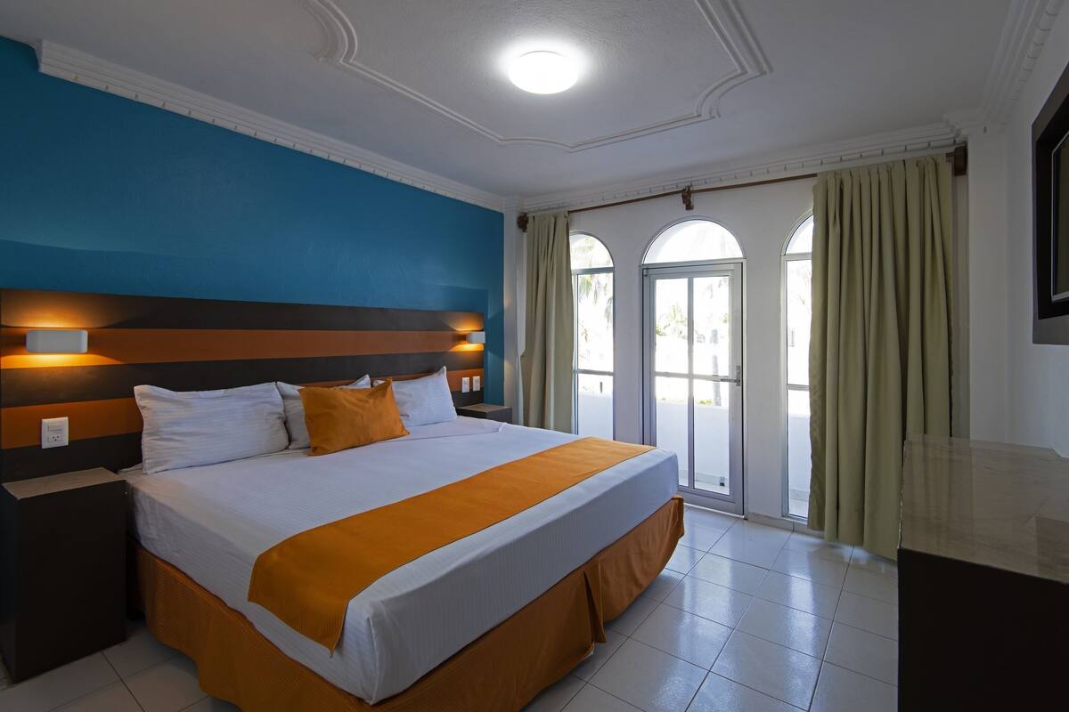 A hotel room with a large bed, a nightstand, a ceiling light, and a view of the outdoors through a glass door.