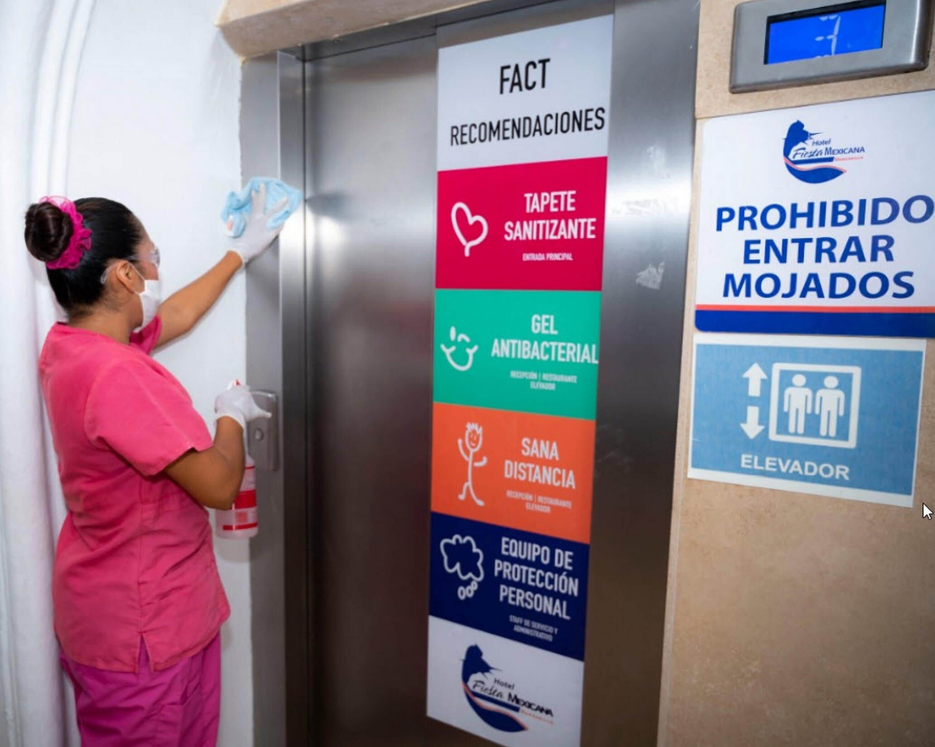 A person sanitizing a door handle in a hotel elevator.
