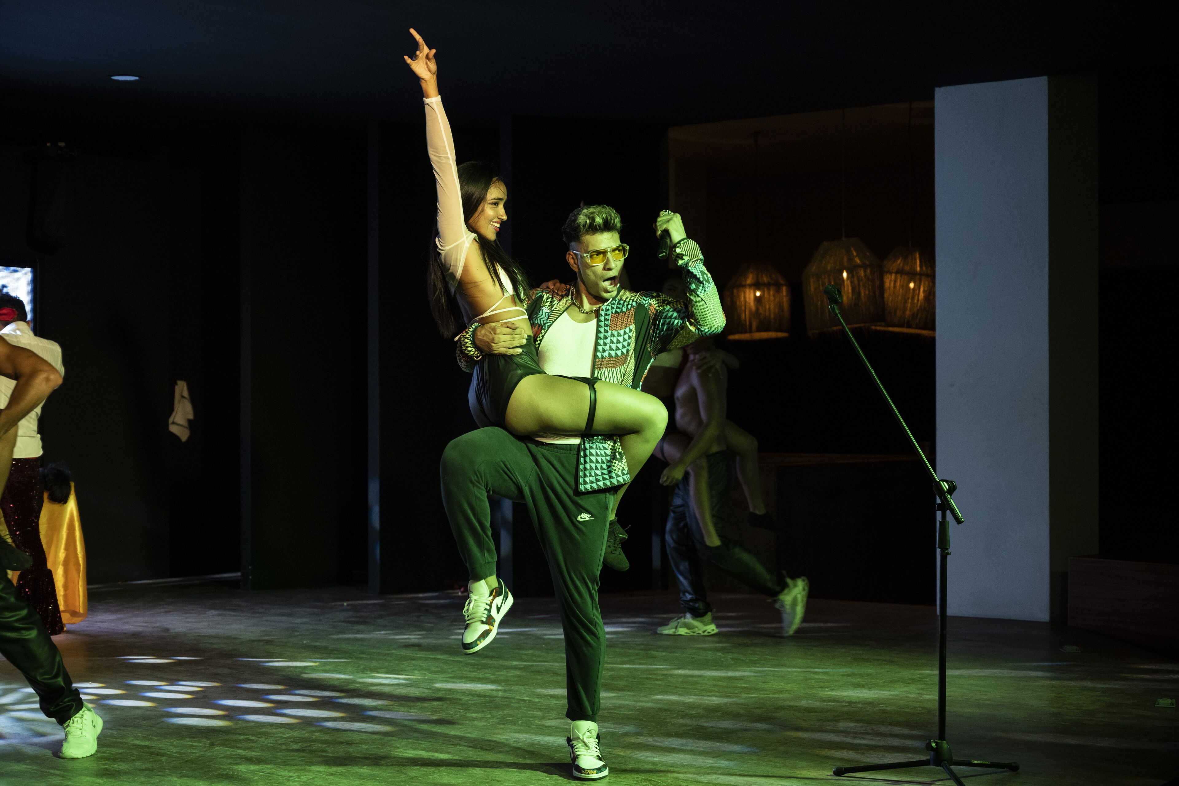 A dance performance in a dimly lit room with a microphone stand and a wooden structure in the background.