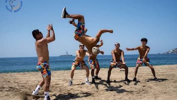 Un grupo de personas jugando voleibol de playa en una arena con un barco al fondo.