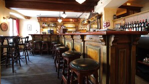 Een bar met houten krukken, een toog en diverse flessen.