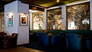 Een restaurant met een rustieke inrichting, met houten balken, afbeeldingen in lijsten aan de muren en grote ramen met uitzicht op een rotsachtig landschap.
