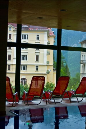 Zona de piscina con sillas rojas y vistas a un edificio con balcones y ventanas.