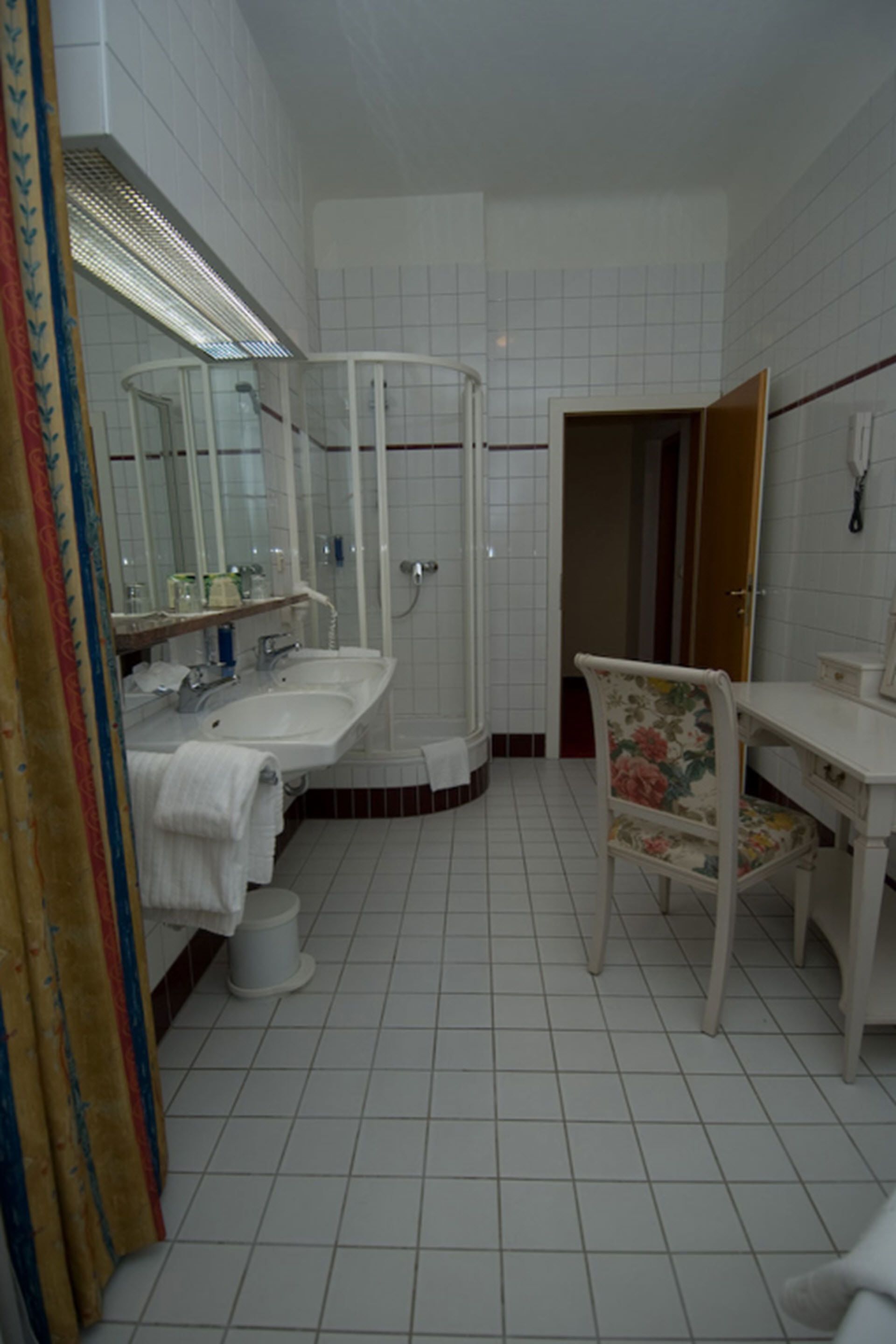 A bathroom with two sinks, a shower, a chair, and a mirror.