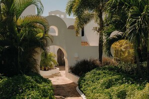 A pathway leading to a building with arches and a white exterior.