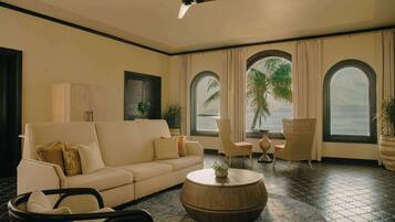 A room with a sofa, chairs, a round coffee table, and large windows with curtains.