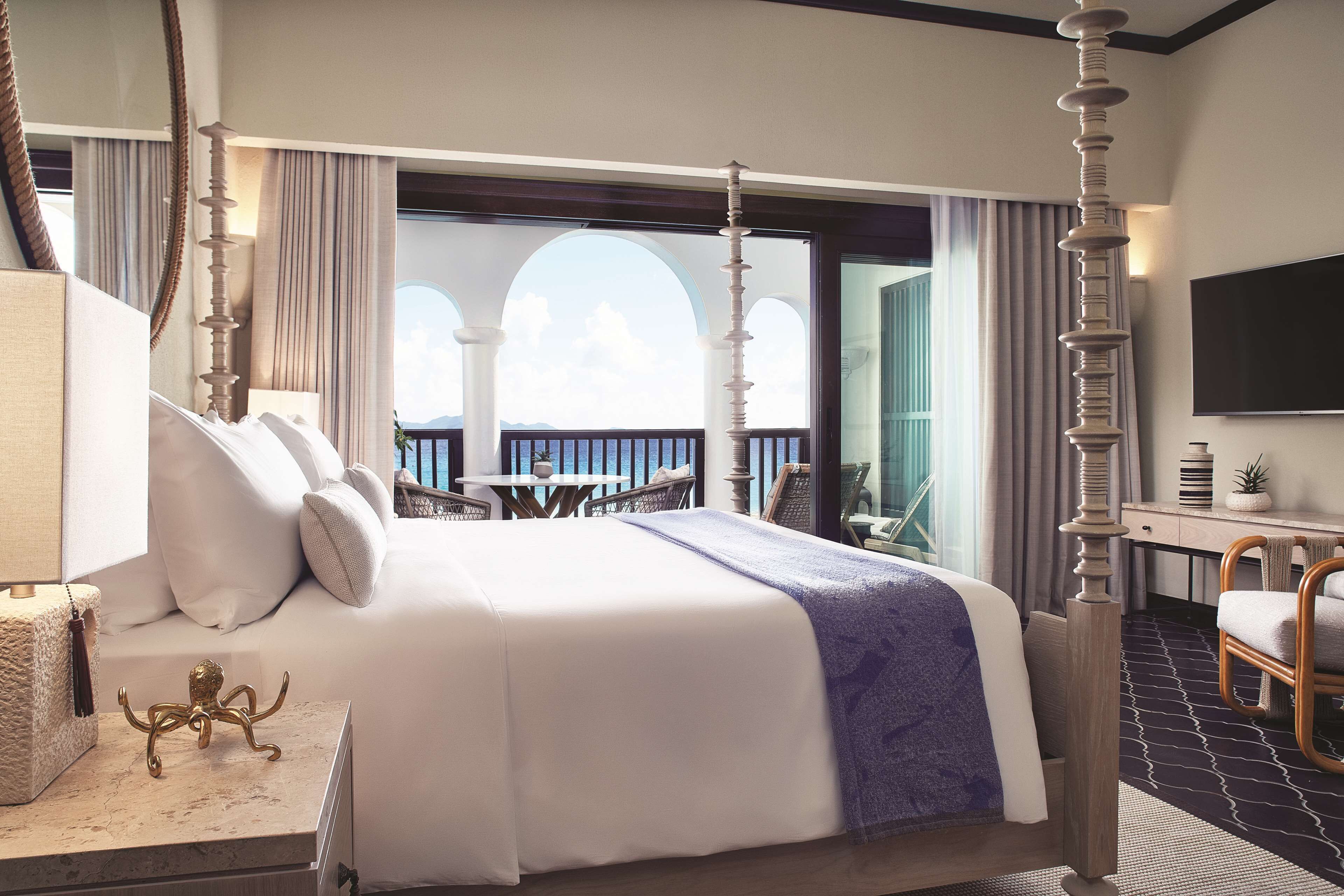 A four-poster bed with a balcony view, a desk with a flat-screen TV, and a chair.