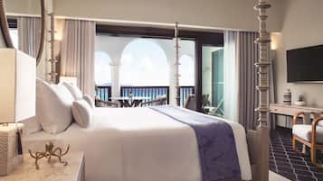 A four-poster bed with a balcony view, a desk with a flat-screen TV, and a chair.
