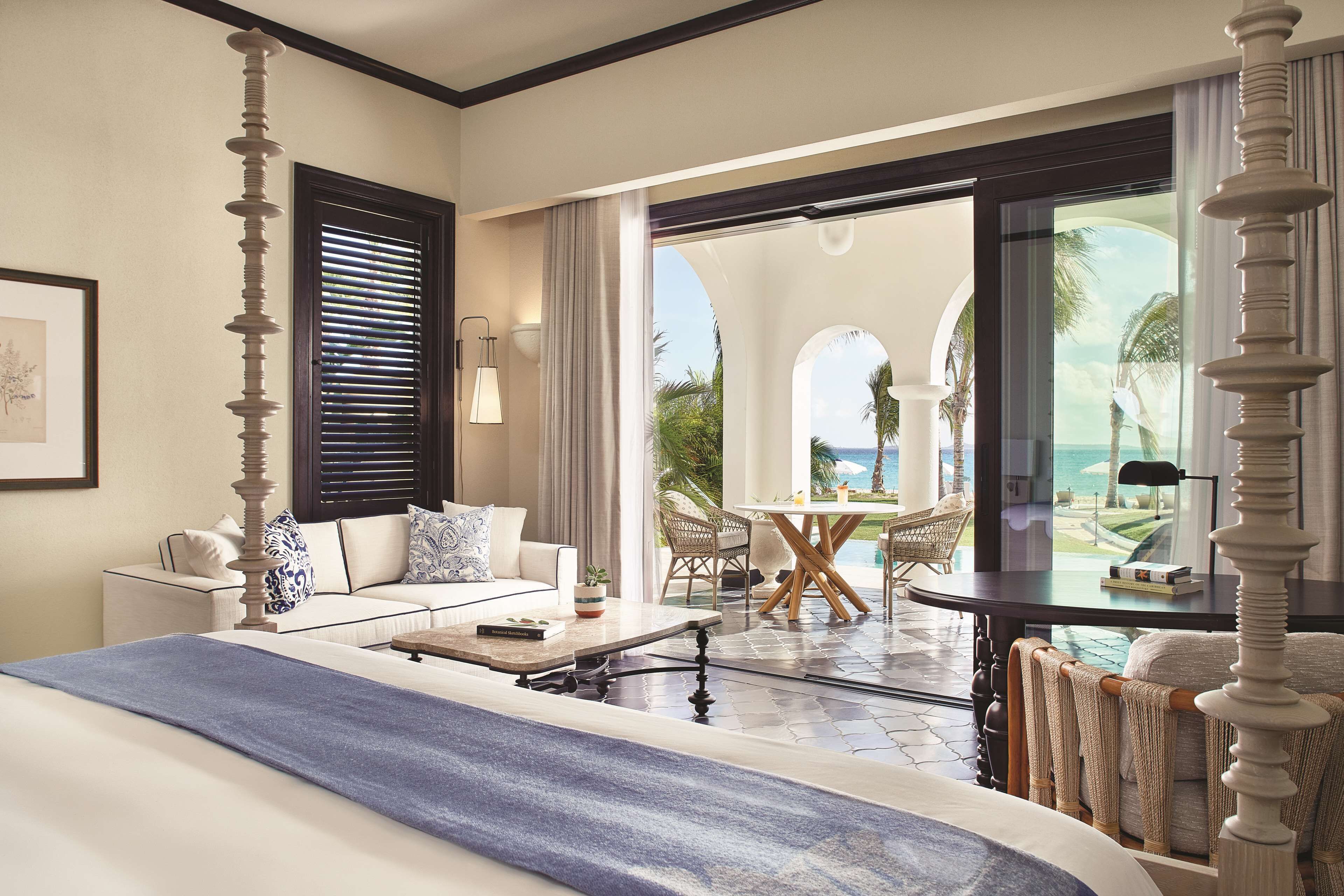 Habitación de hotel con cama, sofá, mesa de comedor y vista al océano.