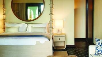 Een hotelkamer met een bed, een ronde spiegel, een nachtkastje met een lamp, een salontafel met een plant en een vloer met een patroon.