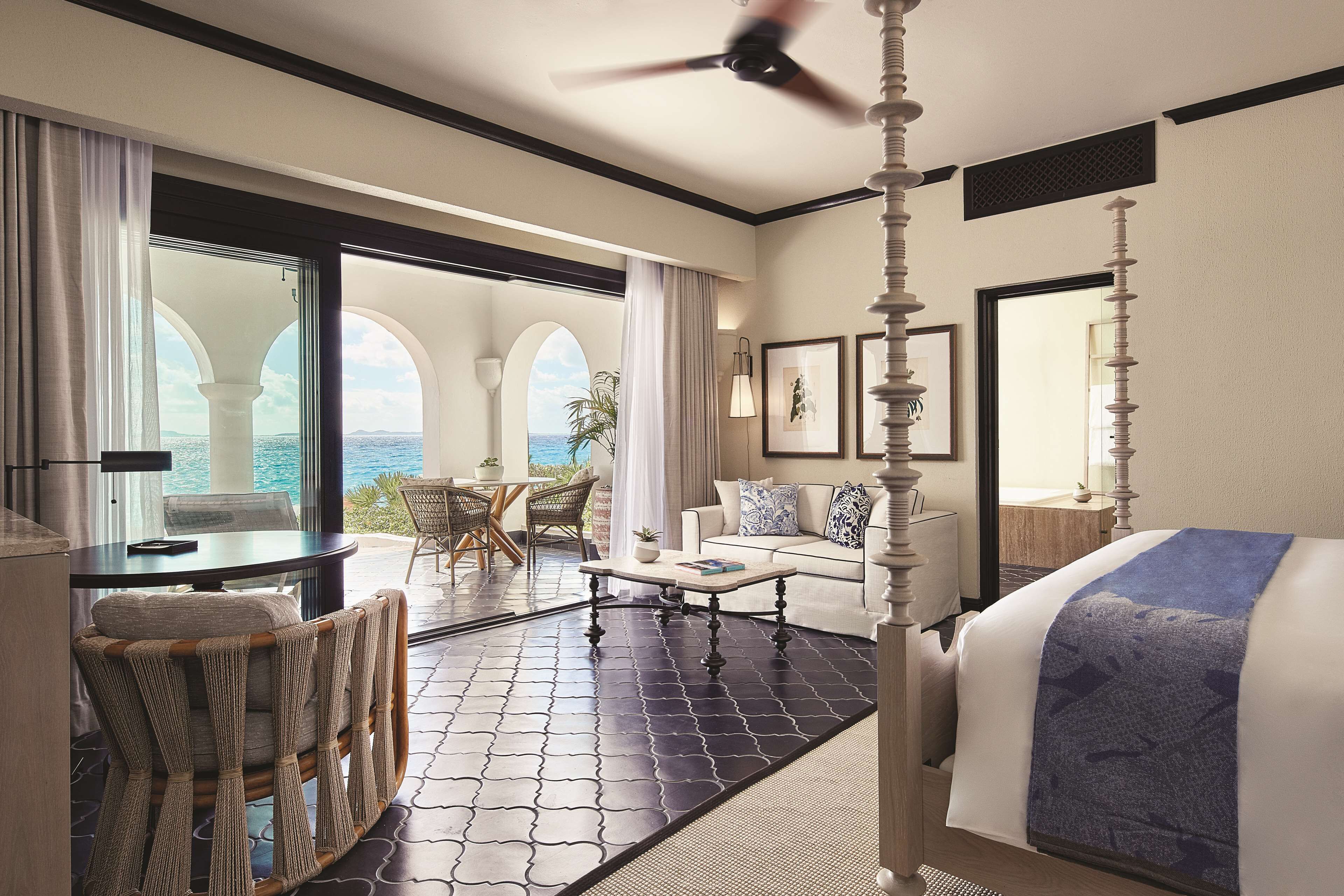 A hotel room with a large bed, a dining table, a sofa, and a view of the ocean.