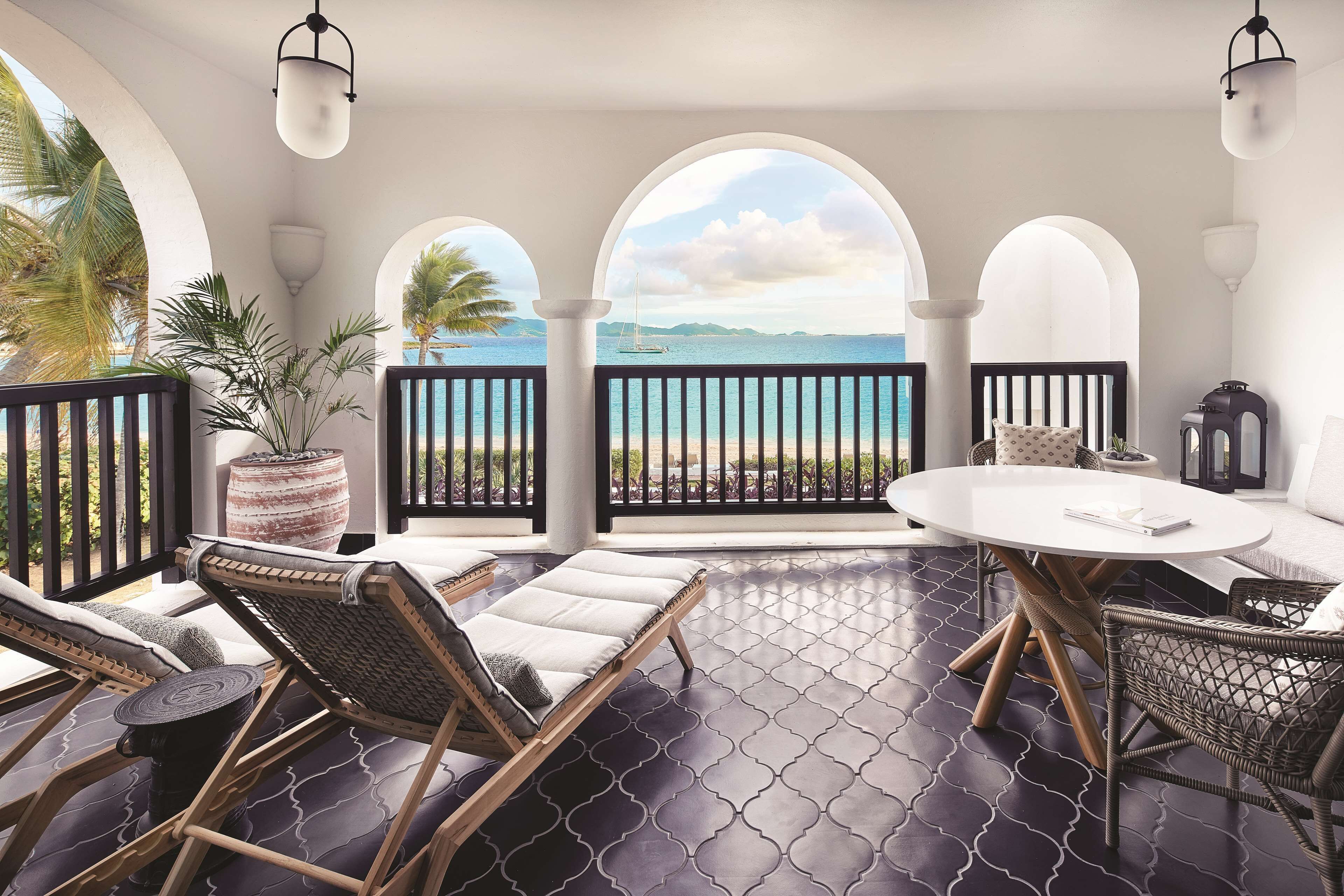 A balcony with a view of the sea, furnished with wicker chairs and a round table.