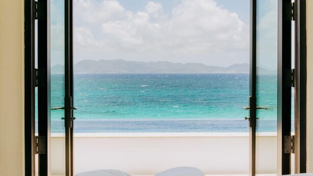 Une chambre avec une grande fenêtre en arc d’où l’on a vue sur une plage et l’océan.
