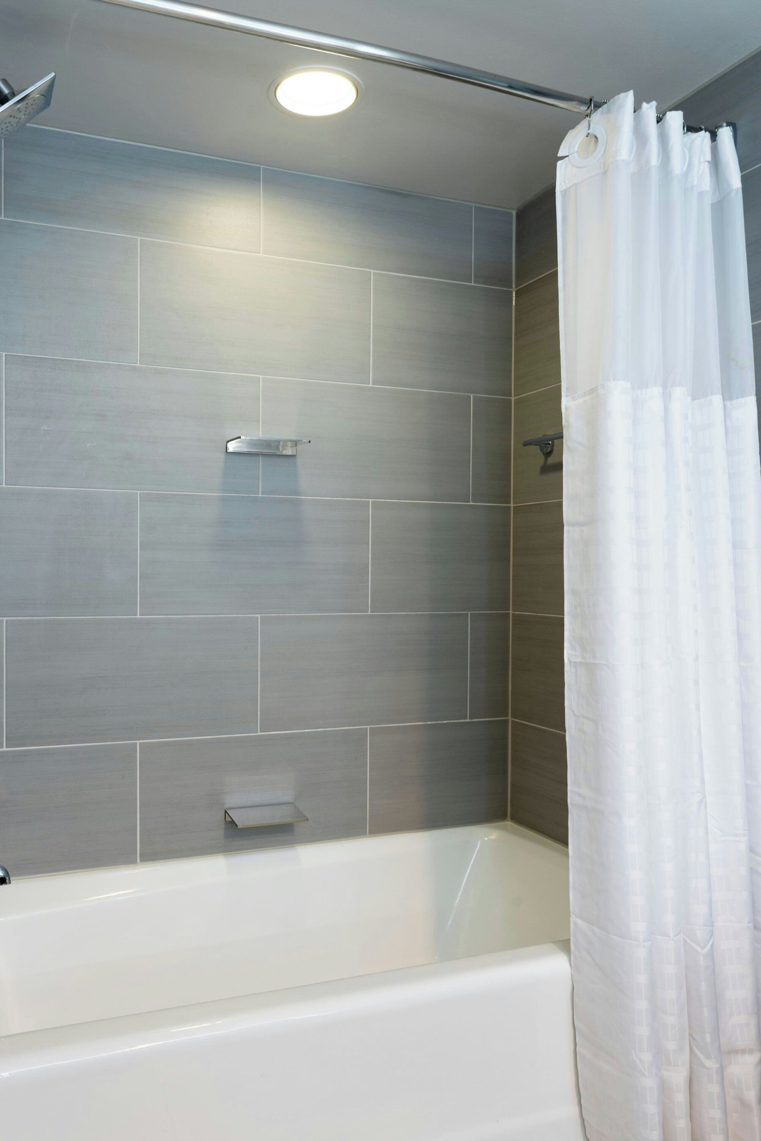 Une salle de bain moderne avec une baignoire blanche, des murs recouverts de carreaux gris et un rideau de douche blanc.