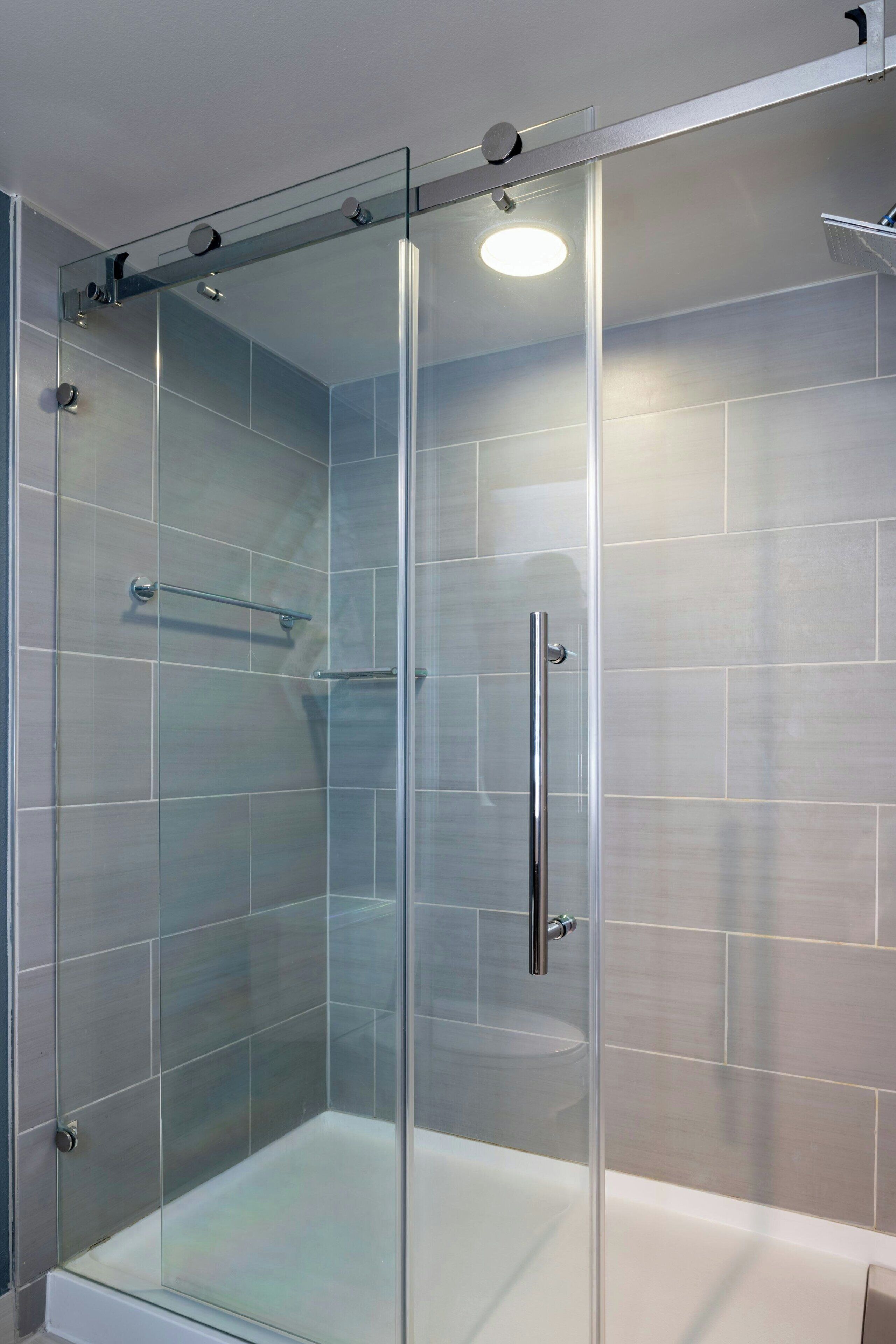 A glass-enclosed shower with a white bathtub, a glass door, and a metal handle.