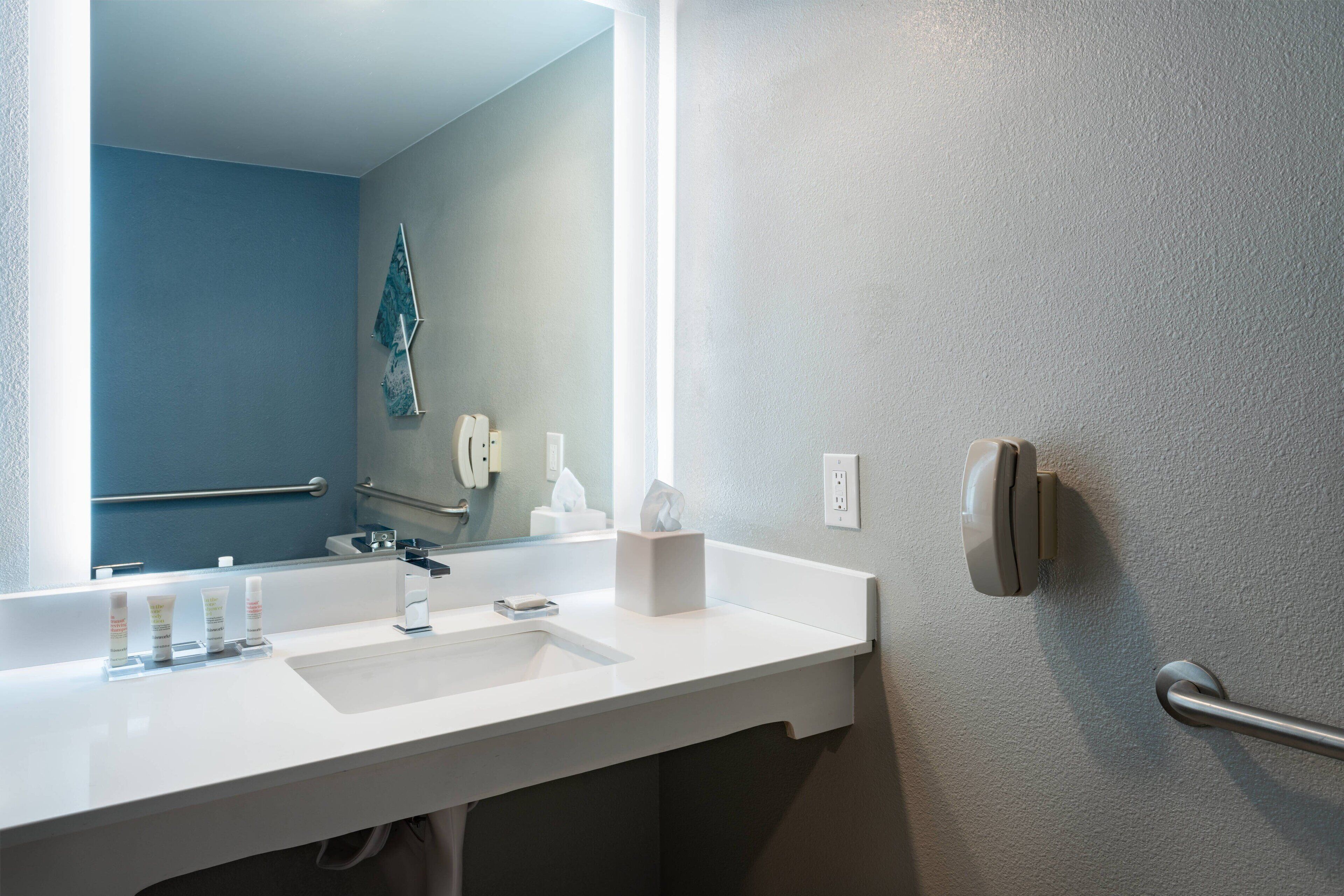 A bathroom with a white sink, a mirror, a towel dispenser, and a hand dryer.