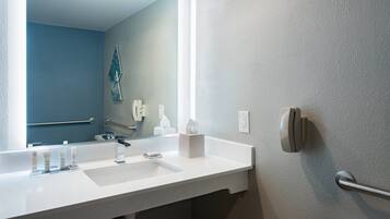 A bathroom with a white sink, a mirror, a towel dispenser, and a hand dryer.