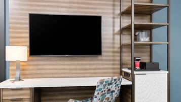 Habitación de hotel con televisión de pantalla plana en la pared, un escritorio con una silla y una cafetera en la encimera.