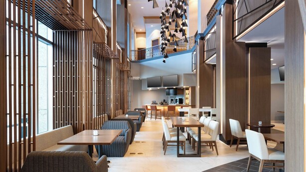 A modern hotel lobby with a high ceiling, a staircase, and a dining area with tables and chairs. - Marriott Anchorage Downtown (Anchorage)