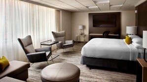 Habitación de hotel con una cama grande, dos sillones, una mesita, un escritorio y un televisor.