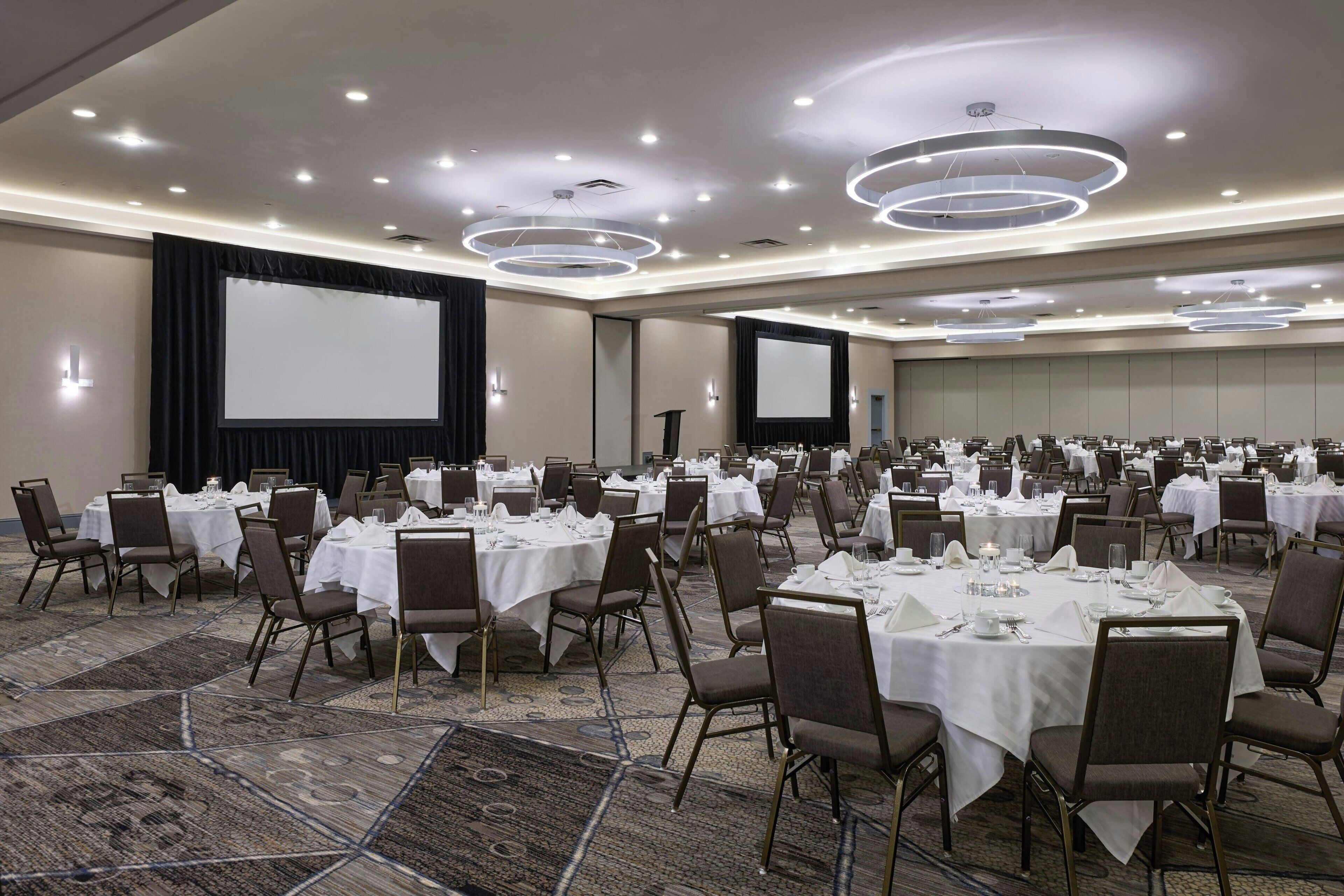 A conference room with multiple tables set for dining, equipped with chairs and white tablecloths.