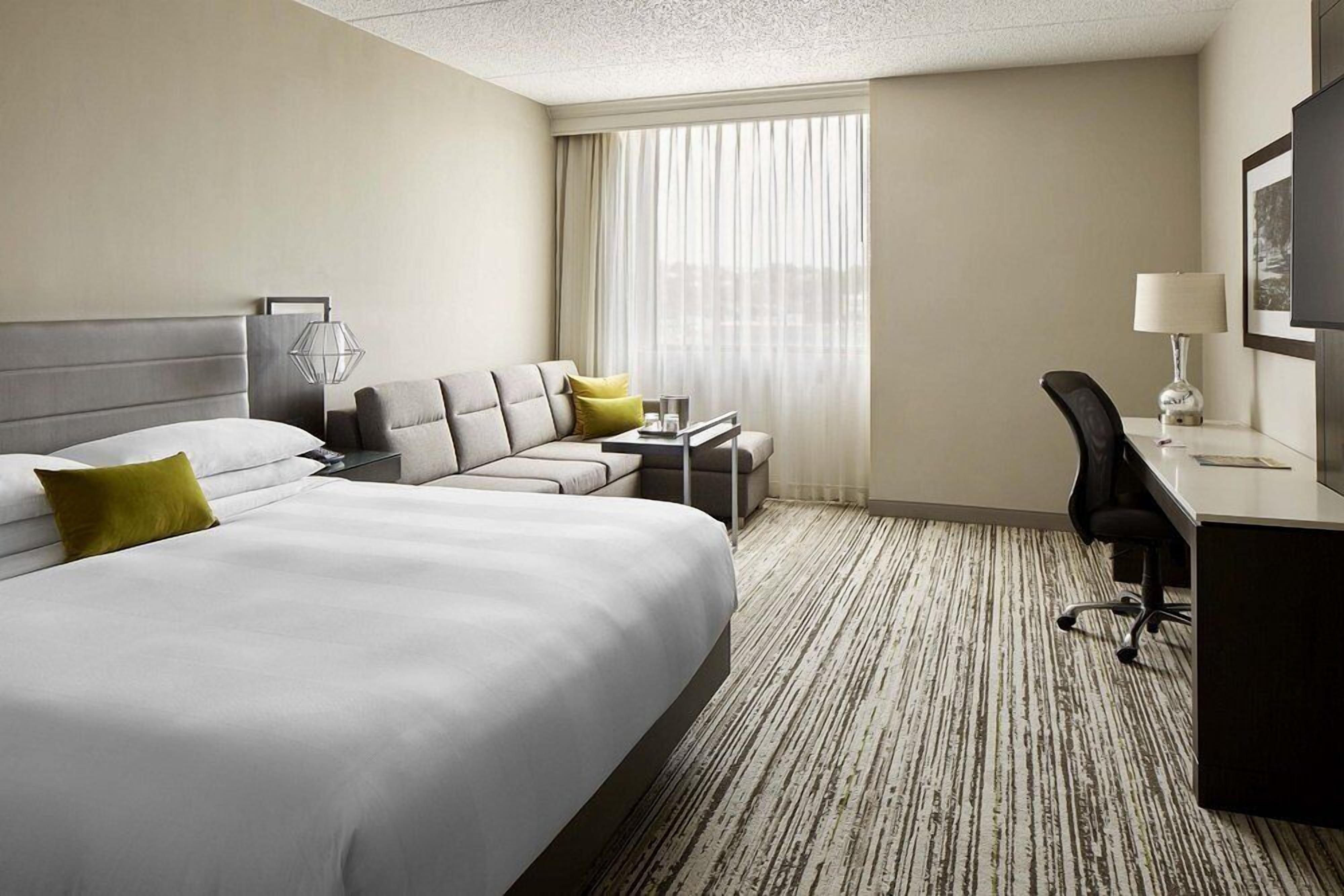 A hotel room with a large bed, a desk, a chair, and a sofa.